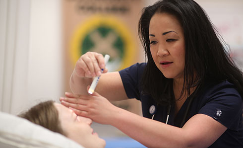 Highline College Nursing Student in lab shining light in eye of student participant